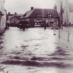 Flooded High Street with tractor 171157 A tractor makes its way past the War Memorial, Pinks store behind